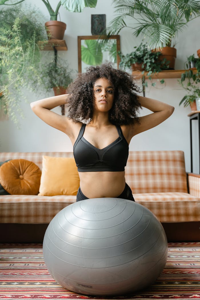 Woman with curly hair exercising with a fitness ball in a plant-filled room.